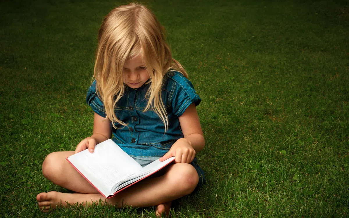 Petite fille faisant la lecture à l'extérieur.